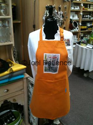 Orange colored apron with a printed front panel displaying a watercolor painting